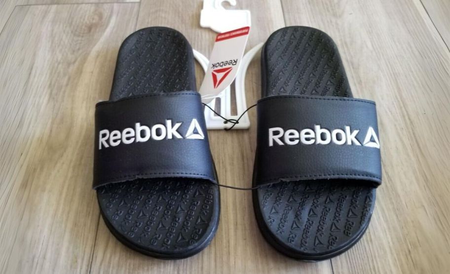 a pair of black reebok mens slides on a hard wood floor