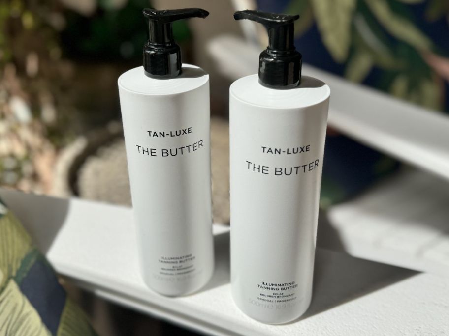 2 Bottles of Tan Luxe the Big Butter set on the arm of a chair in the sun