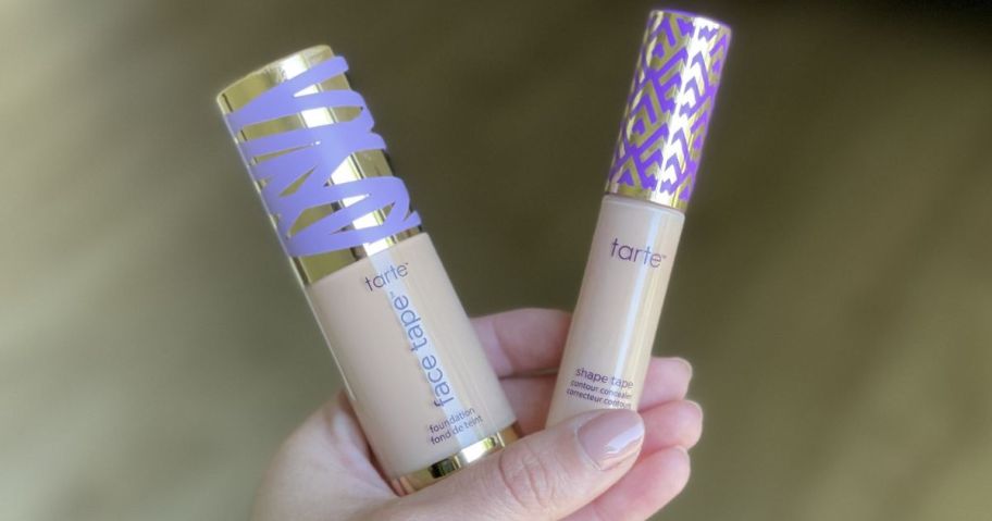 Hand holding tubes of Tarte Face Tape Foundation and Shape Tape Concealer