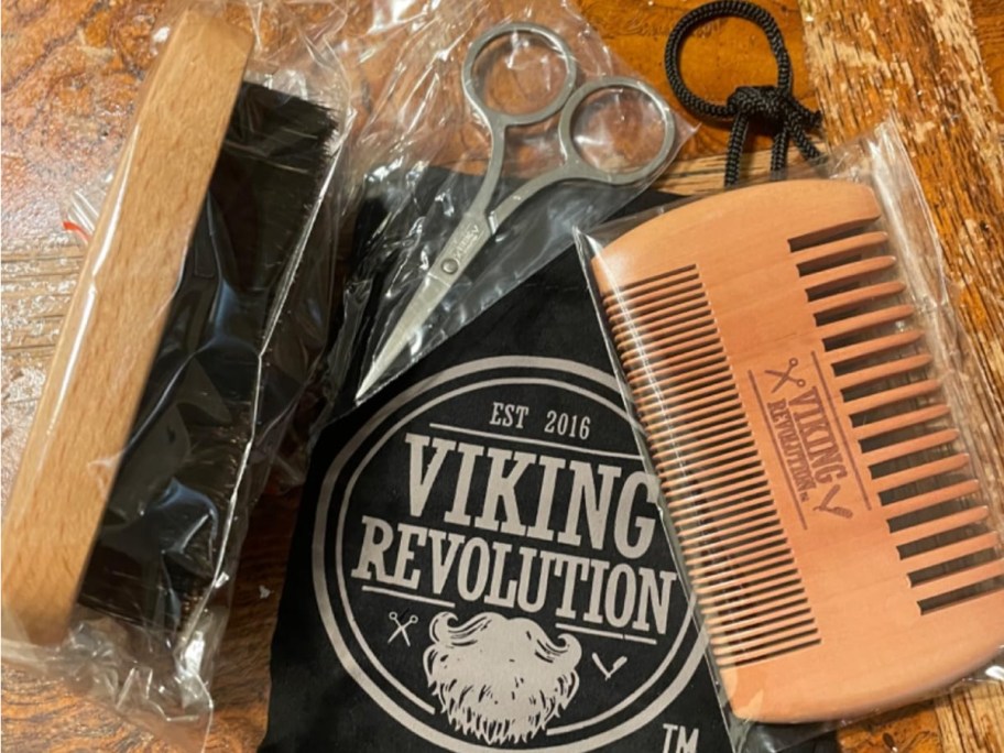 A Viking Revolution beard brush, scissors, and onlineb laying on a storage bag with the Viking Revolution logo on it