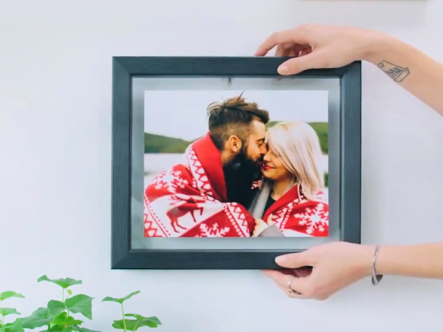 Person hanging black floating frame on wall featuring a man and a woman