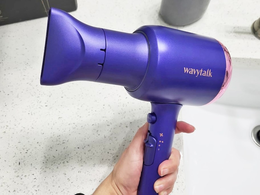 hand holding a purple hair dryer in bathroom