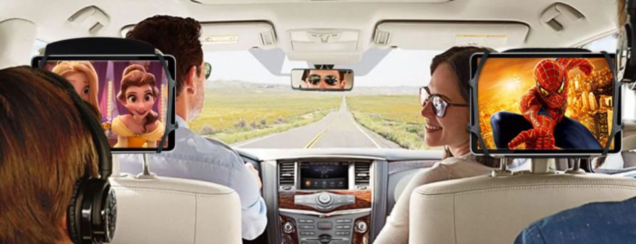 inside a family suv with point of view from the back of the vehicle showing two kids in back seat each with a tablet holding thei devices, while mom and dad are in front seat.