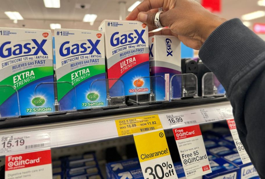 a womans hand grabbing a box of gas x off a store shelf