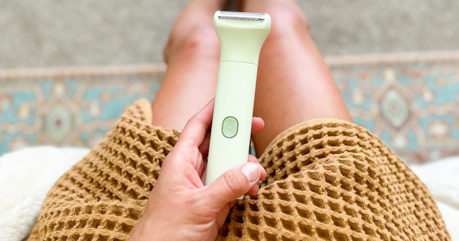 hand holding mint colored bikini trimmer above legs 