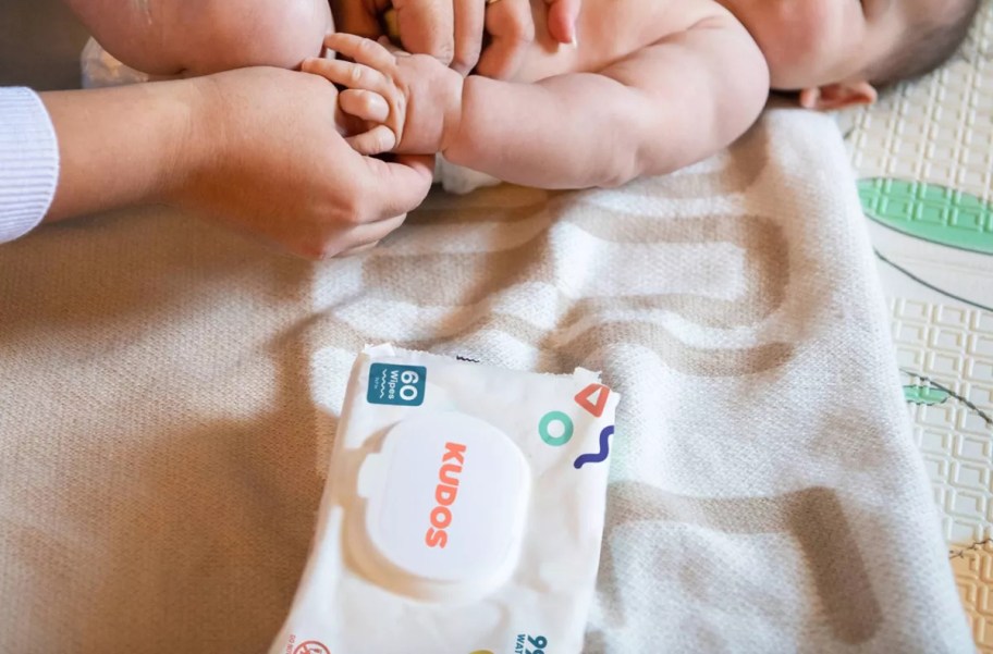 kudos baby wipes on blanket with mom changing baby's diaper