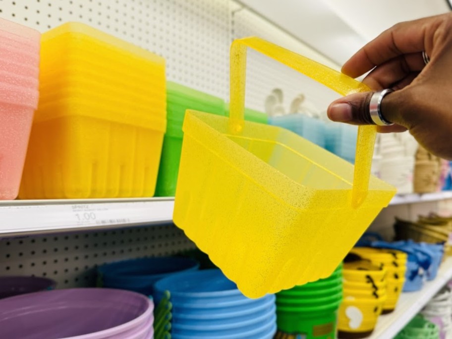 hand holding a yellow berry basket style Easter Basket, more colors of the basket on a shelf behind it