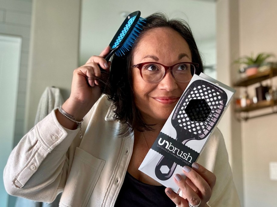 Lina brushing her hair with an UNbrush hair brush while holding another brush in it's packaging box in the other hand