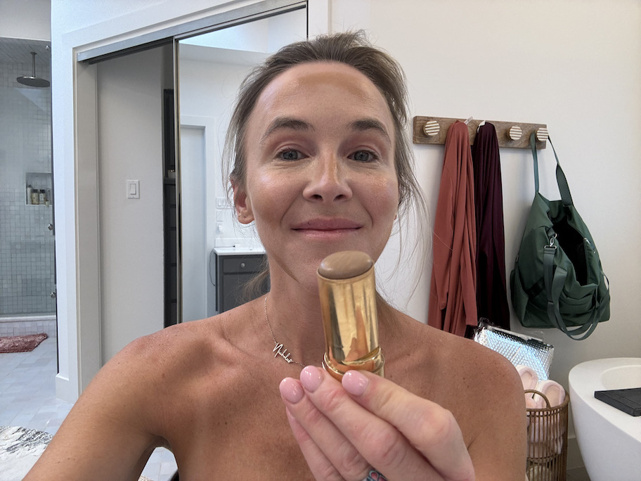 woman putting on merit bronzer sitting in bathroom