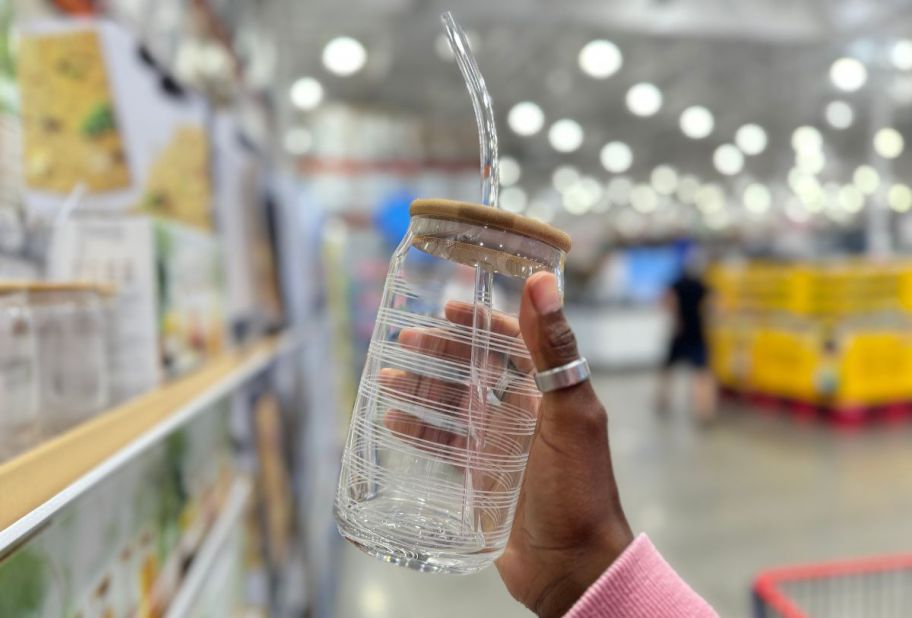 a womans hand displaying a ;arge glass tumbler with lid