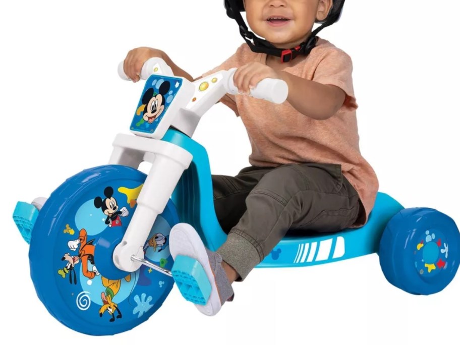 a little boy riding a blue and white low ride tricycle that has Mickey Mouse decals on it