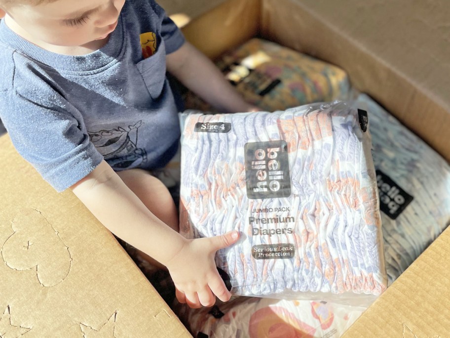 Baby sitting in a box holding a pack of Hello Bello diapers