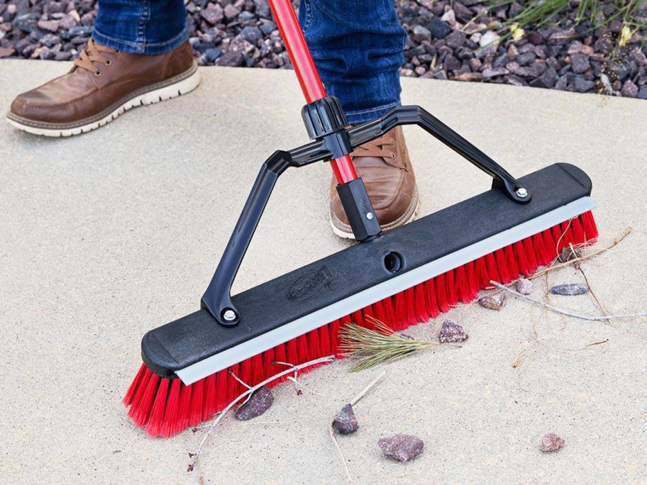 man cleaning sidewalk with red and black push broom