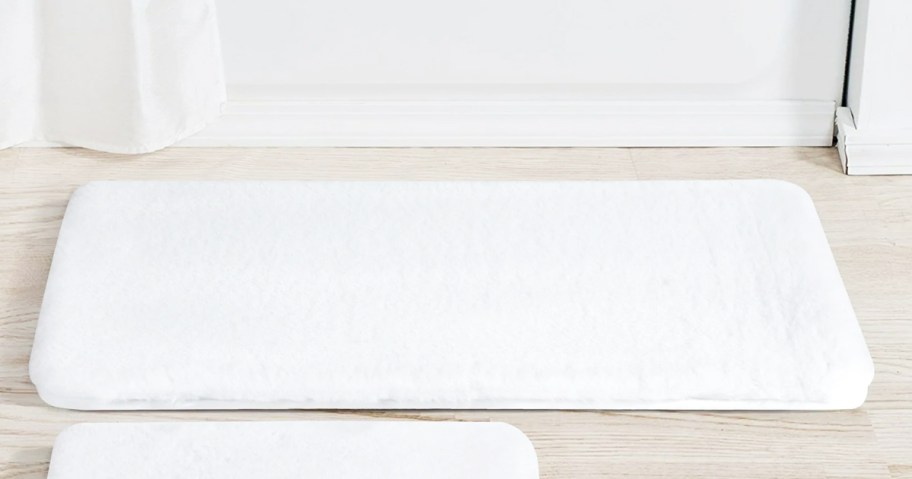 white bath rug in front of a tub