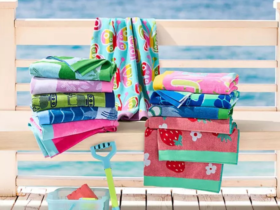 Colorful kids, beach towels stacked up on white wooden bench in front of ocean