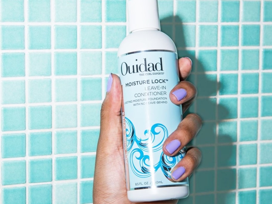 hand holding up a bottle of Ouidad Moisture Lock Leave-in Conditioner in shower