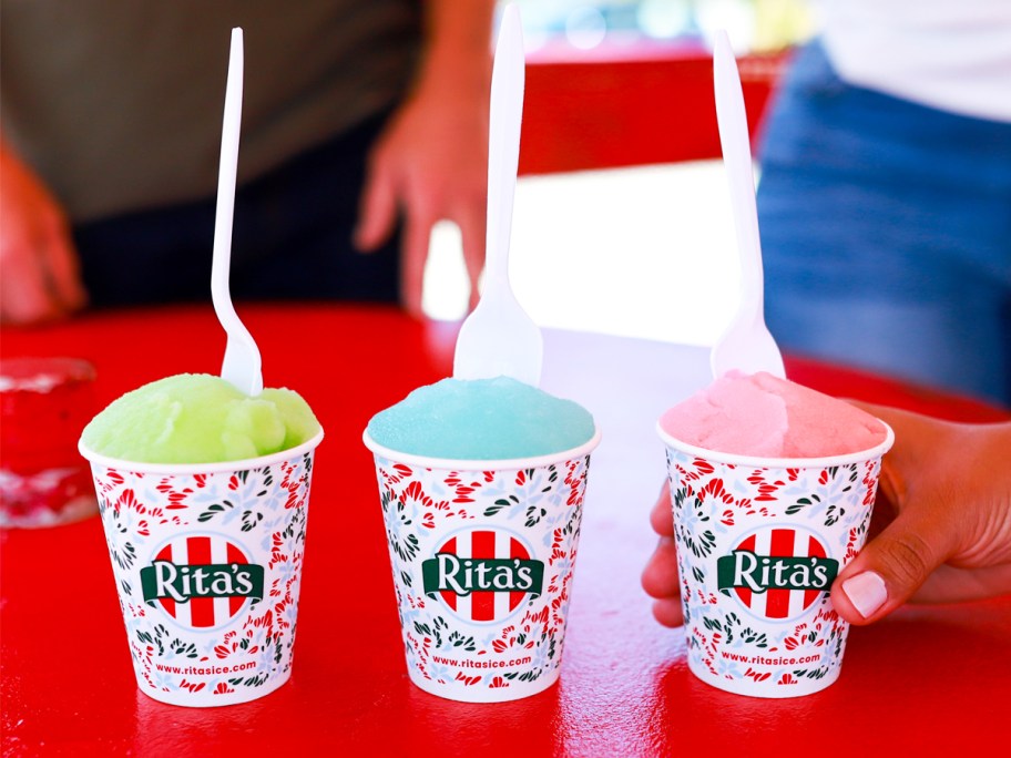 green, blue, and red cups of Rita's Italian Ice on red table