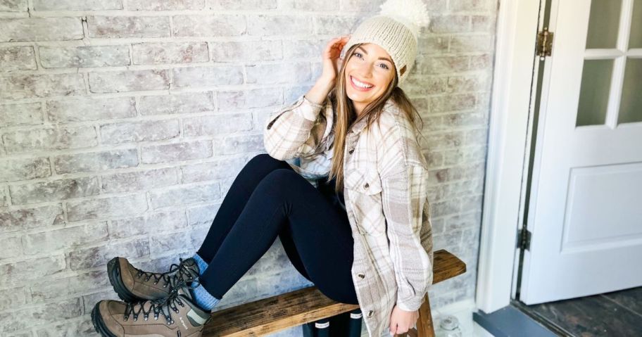 Woman wearing a SO shacket and a cozy pom pom hat while sitting on a bench