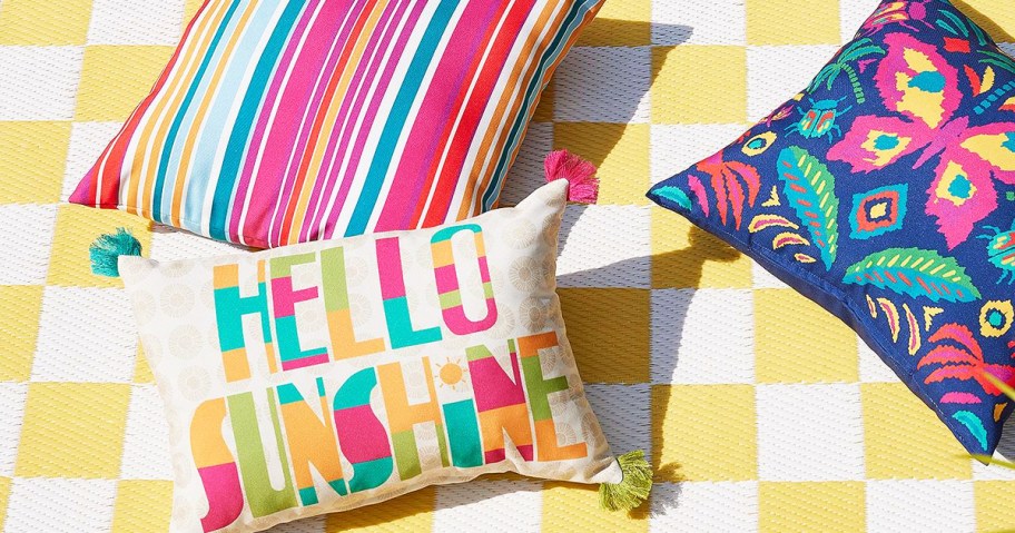 3 brightly colored outdoor throw pillows on a white and yellow checkered outdoor rug