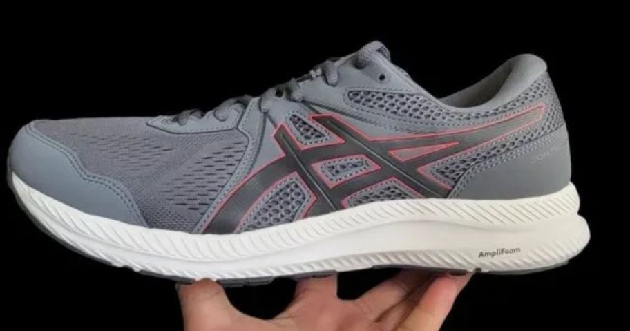 a mans hand holding a gray asics gel contend 8 running shoe