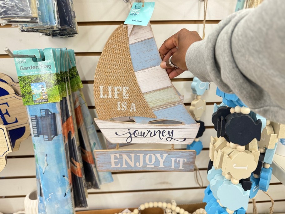 hand reaching for a sailboat shaped beach decor sign