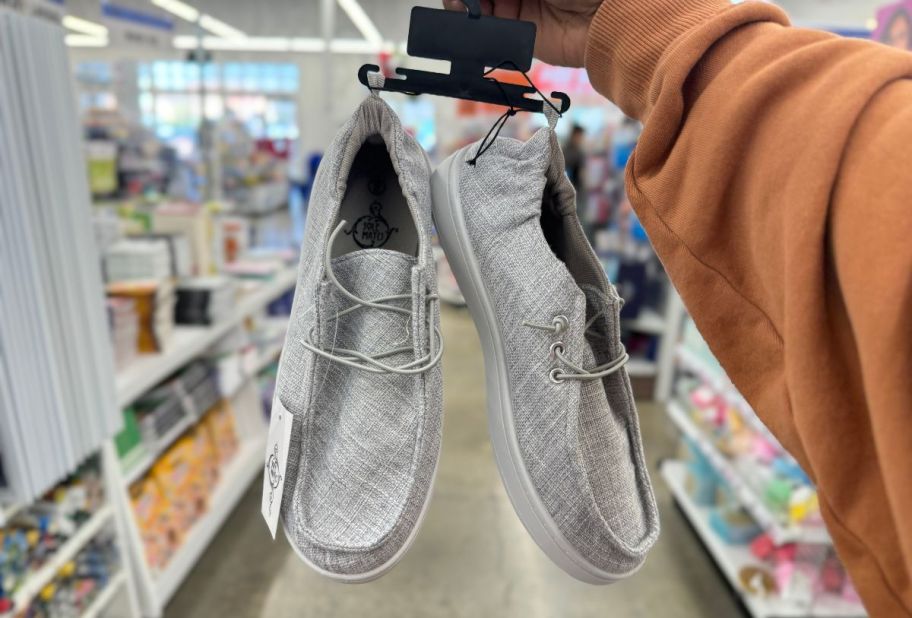 a womans hand holding a pair of grey lace up casual shoes