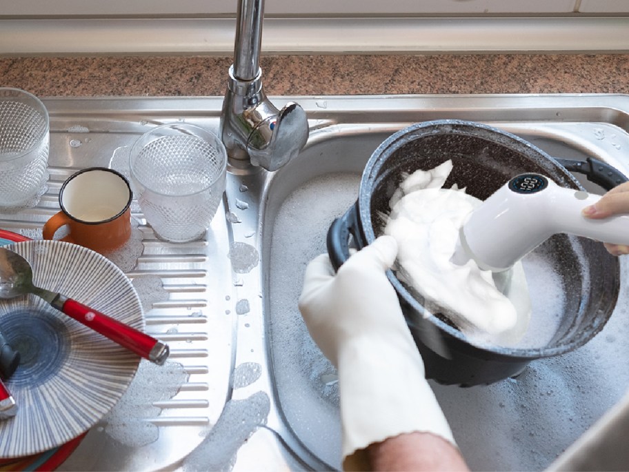  hand holding electric spin brush while washing dishes