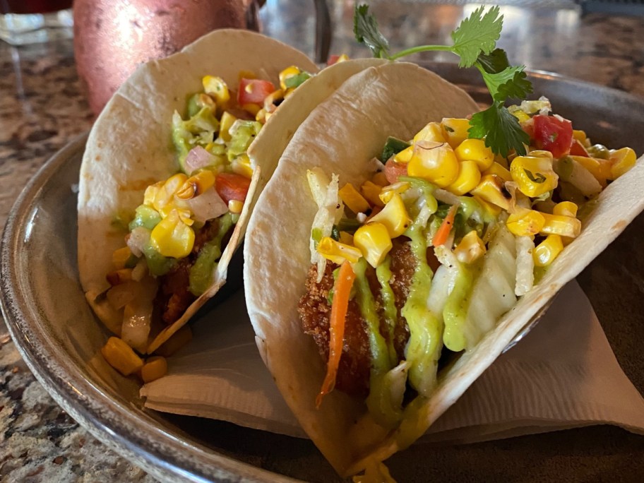 two fish tacos next to a copper mug