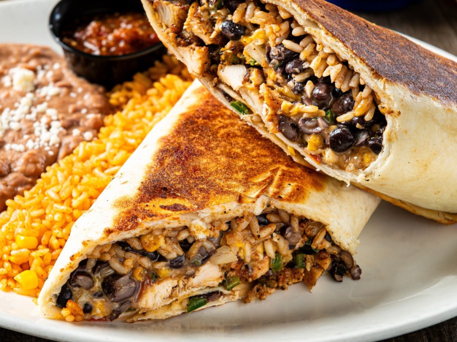 burrito cut in half on a plate with beans and salsa