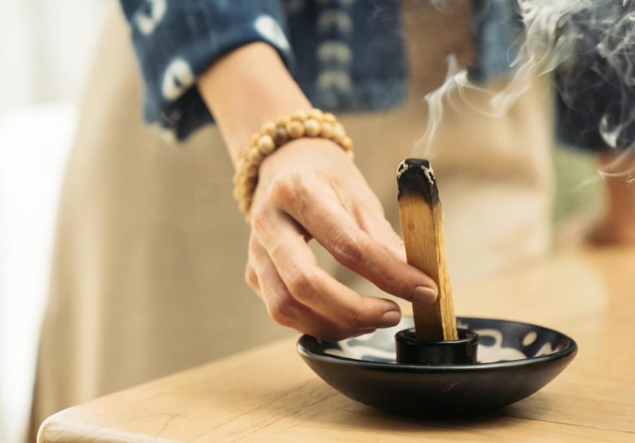 hand holding palo santo stick over bowl