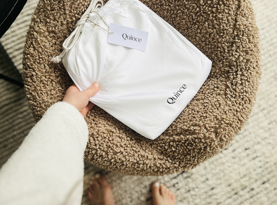 hand holding a quince bag of white sheets on furry ottoman