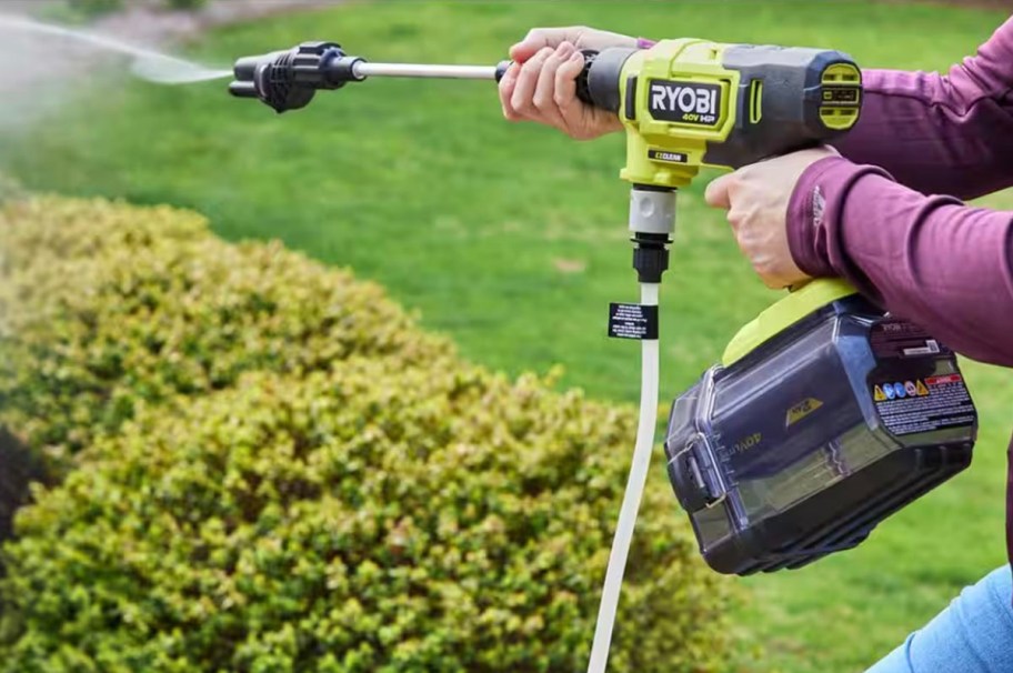 hands holding ryobi power washer spraying bushes