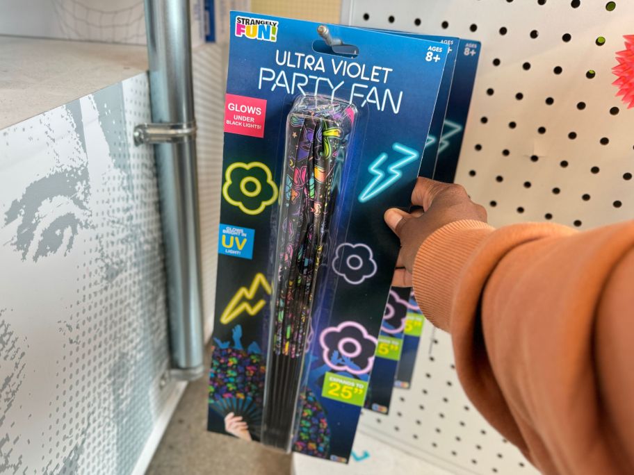 a womans hand grabbing a uv party fan from a peg on a store aisle