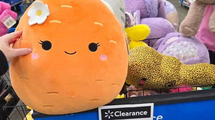 a large orange Squishmallow plush with more in a bin behind it