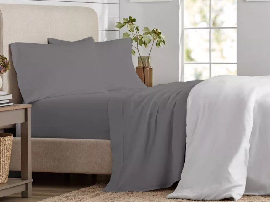 bed with onlineforter pulled back showing grey sheets and pillows