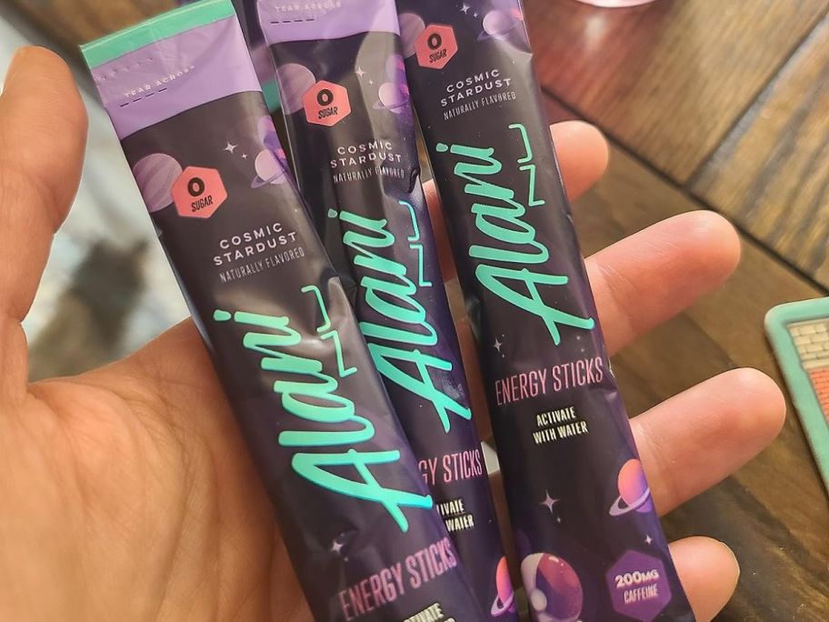 hand holding 3 Alani Nu Energy Sticks