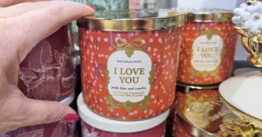 hand touching a red Bath & Body Works 3-Wick Candle that says "i love you"