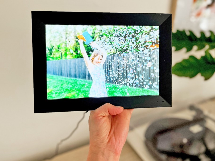 hand holding up a black digital picture frame with photo of girl surrounded by bubbles