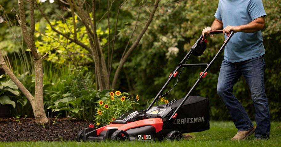 man pushing red and black lawn mower