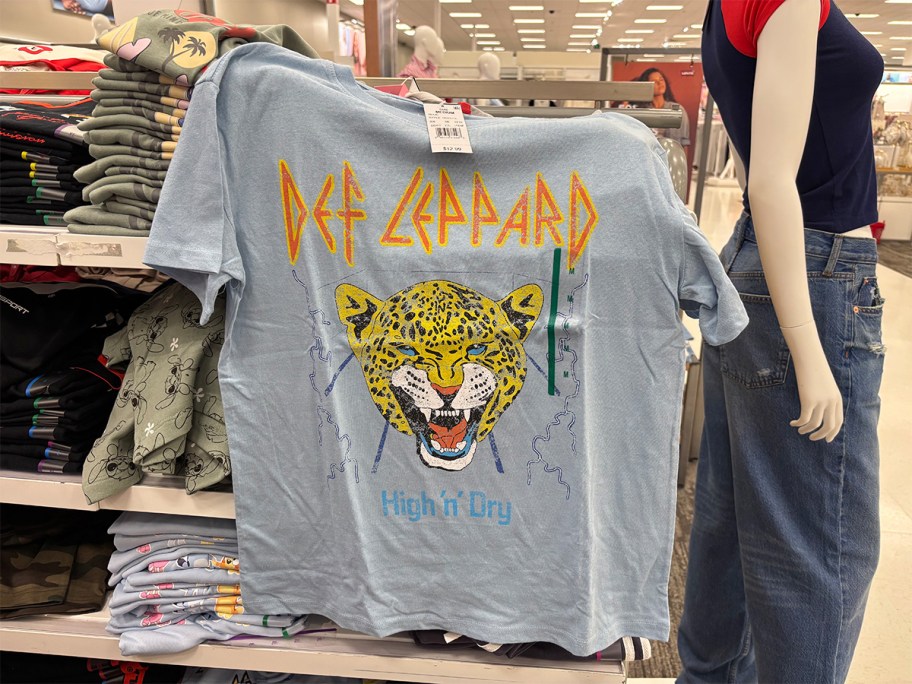 Light blue Def Leppard band T-shirt at Target featuring a roaring leopard graphic and “High ’n’ Dry” text, displayed on a store rack.