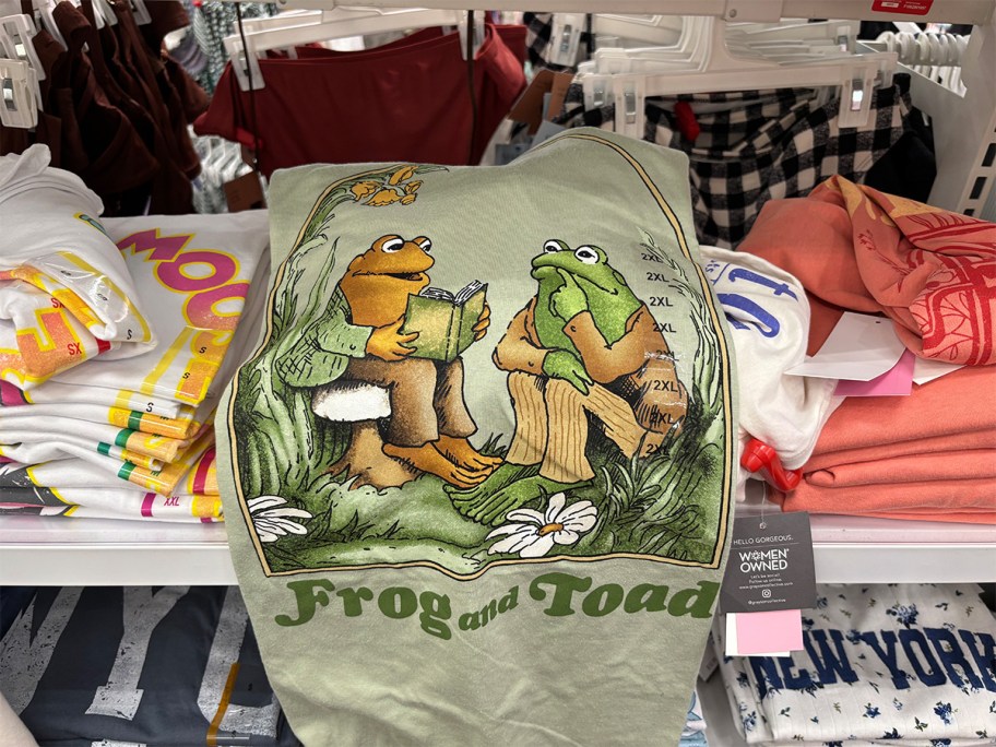 Green Frog and Toad graphic T-shirt at Target featuring the classic characters reading and thinking, displayed on a store shelf.