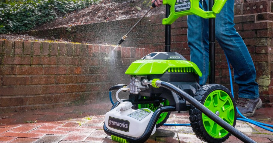 man using green and black pressure washer on brick