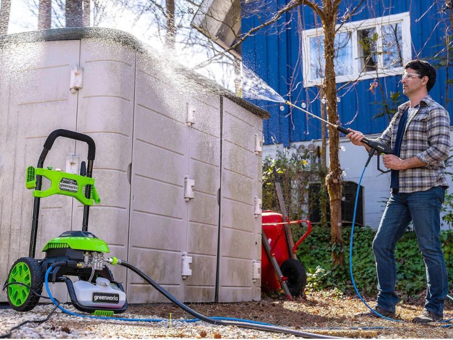 man using a Greenworks pressure washer to clean a shed