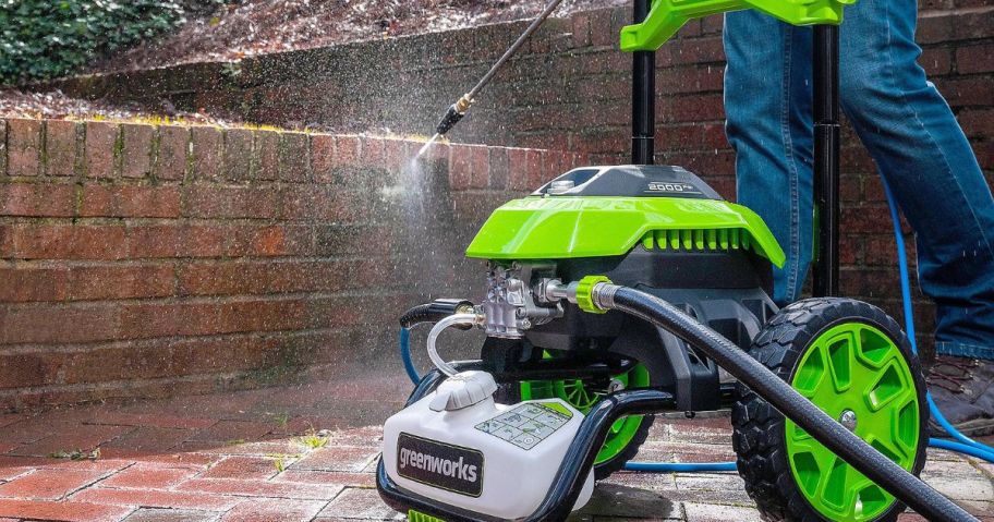 Someone using a greenworks Pressure Washer to clean a brick wall