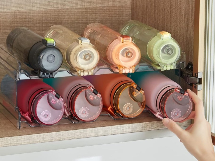 hand reaching for a water bottle on a plastic 2 tier water bottle organizer in a cabinet