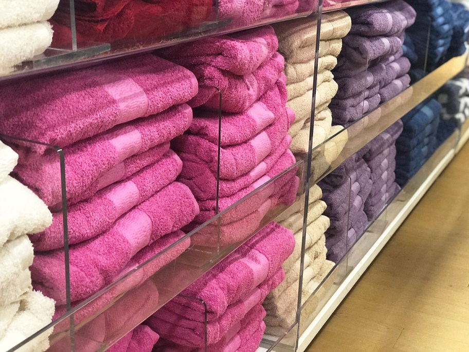 folded stacks of pink, beige, and purple bath towels on store display shelves