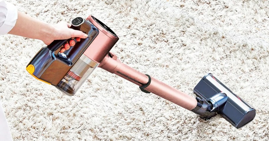 woman using rose gold stick vacuum on white carpet