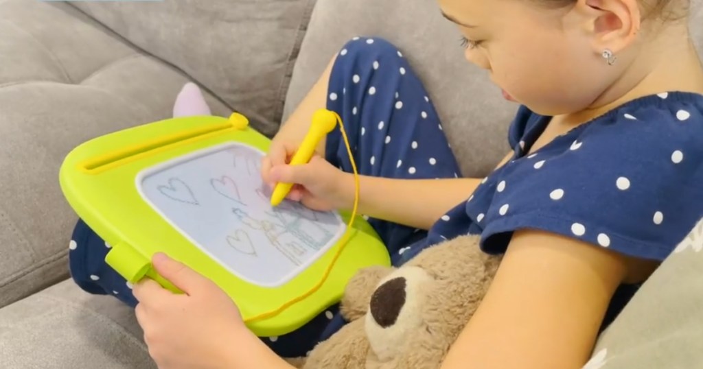 little girl drawing on board on couch