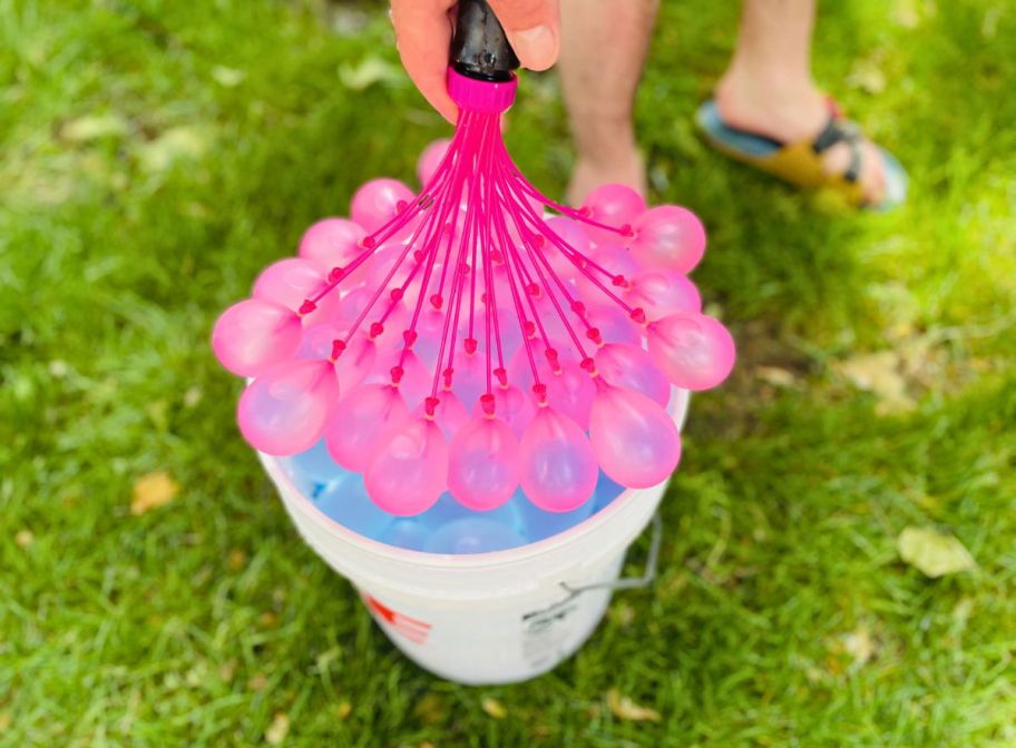 pink water balloons being filled with a hose over a five gallon bucket