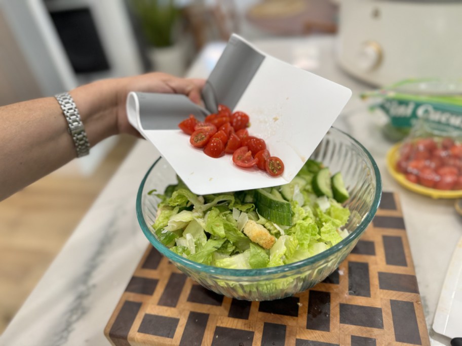 Hand using the scooperduper to place tomatoes into a salad bowl